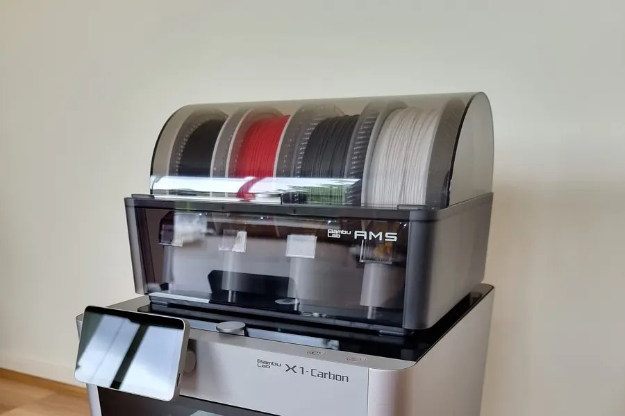 A Bambu Lab X1 Carbon printer with a four spool AMS unit on top, its lid closed over black, red, grey and white filament