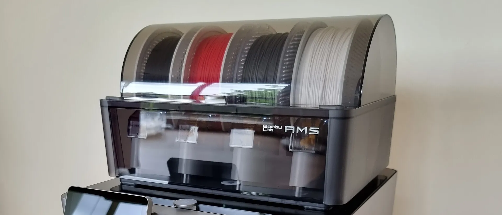 A Bambu Lab X1 Carbon printer with a four spool AMS unit on top, its lid closed over black, red, grey and white filament