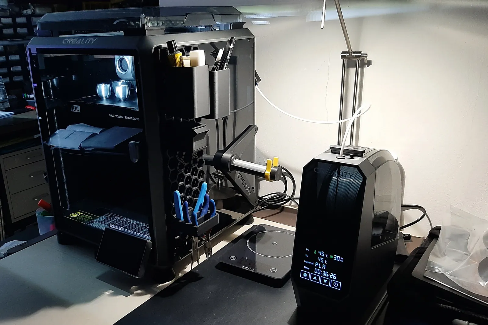 A filament dry box beside a printer, a spool behind its window and the display reading 45 degrees and 45 per cent
