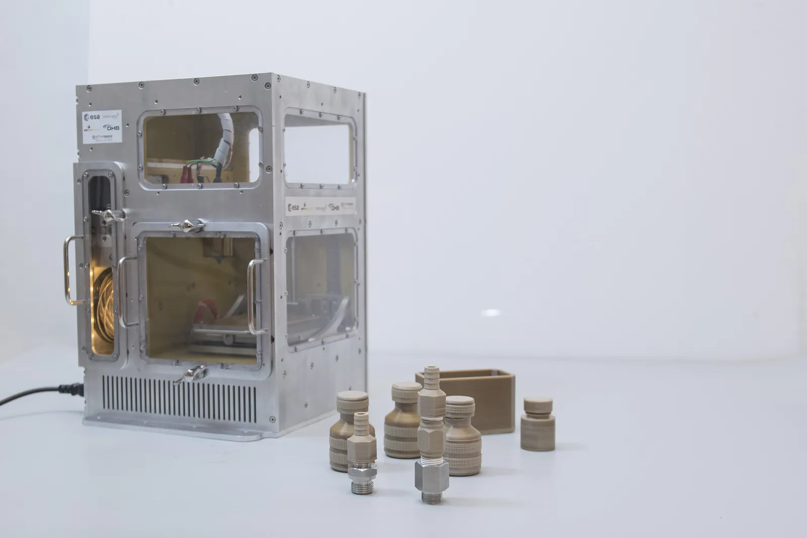 ESA's MELT printer, an aluminium boxed machine, with beige printed fittings and a small box in front of it