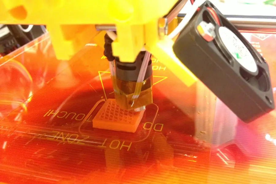 A printer nozzle laying down orange plastic over a heated bed