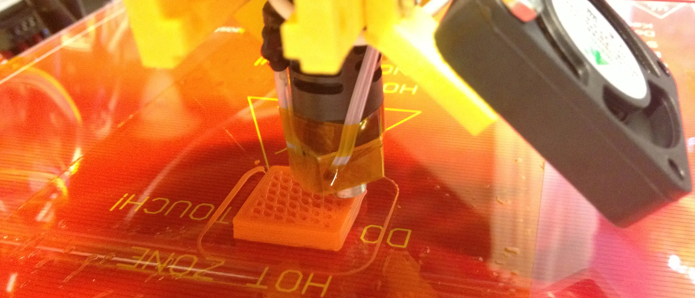 A printer nozzle laying down orange plastic over a heated bed