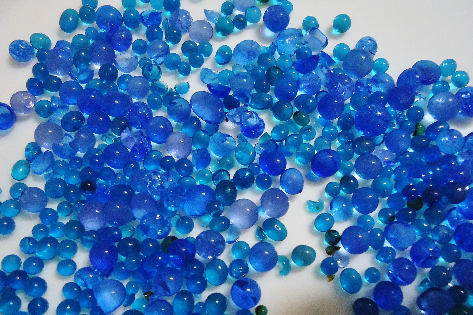 Translucent blue silica gel desiccant beads scattered on a white surface