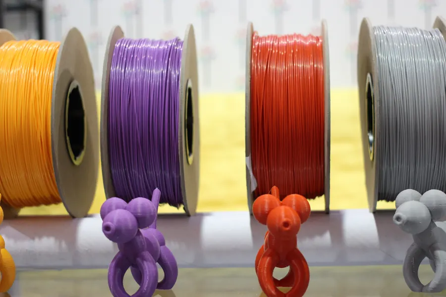 Spools of orange, purple, red and grey filament on a shelf above printed figurines