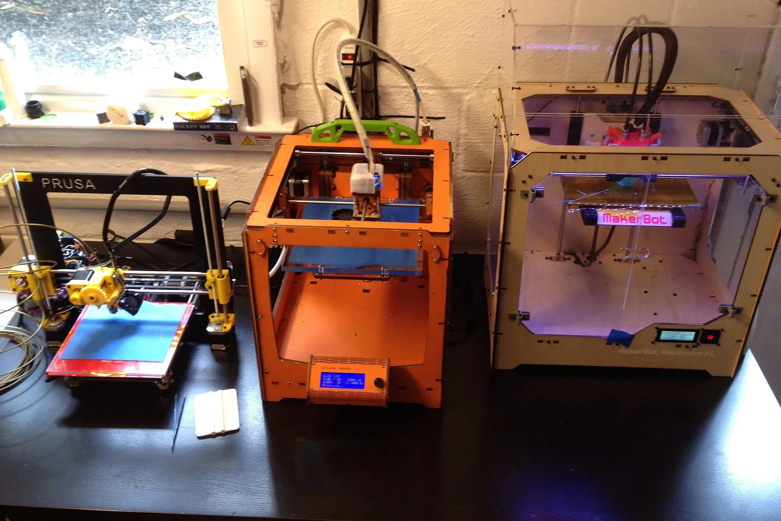 An open-frame printer beside two enclosed hobbyist printers